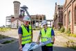 Die beiden zuständigen Projektingenieure der RAG Montan Immobilien Kai Kopke und Andreas Boermann. Im Hintergrund links das Schachtgerüst Heinrich mit der Schachthalle und dem Grubenlüfter, die zurückgebaut werden. Die Gebäude auf der rechten Seite (Grubenmagazin und Maschinenzentrale) bleiben erhalten. Foto: RAG Montan Immobilien GmbH/Holger Jacoby